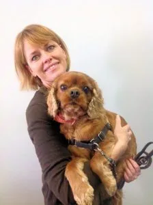 A woman holding a dog with scissors in her hand.