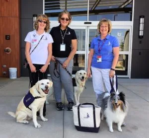 Three women with service dogs outside a building.