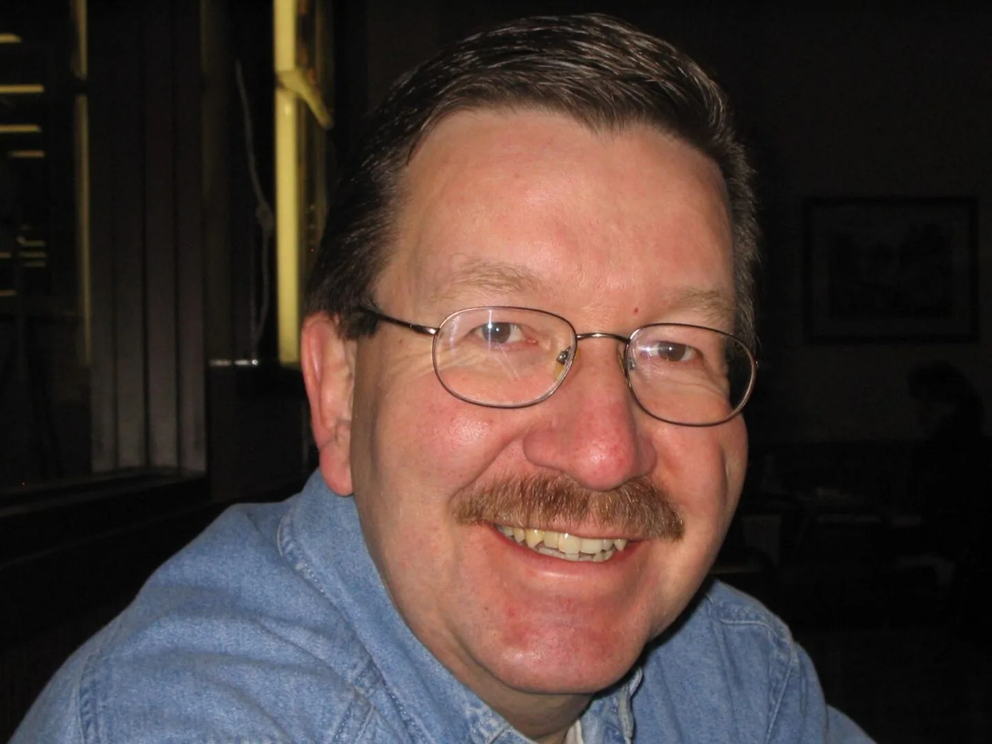 Smiling man with glasses wearing a blue shirt.