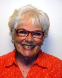 A woman with white hair and glasses smiling.