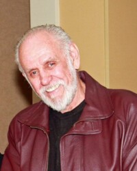 A man with white hair and beard wearing a red jacket.